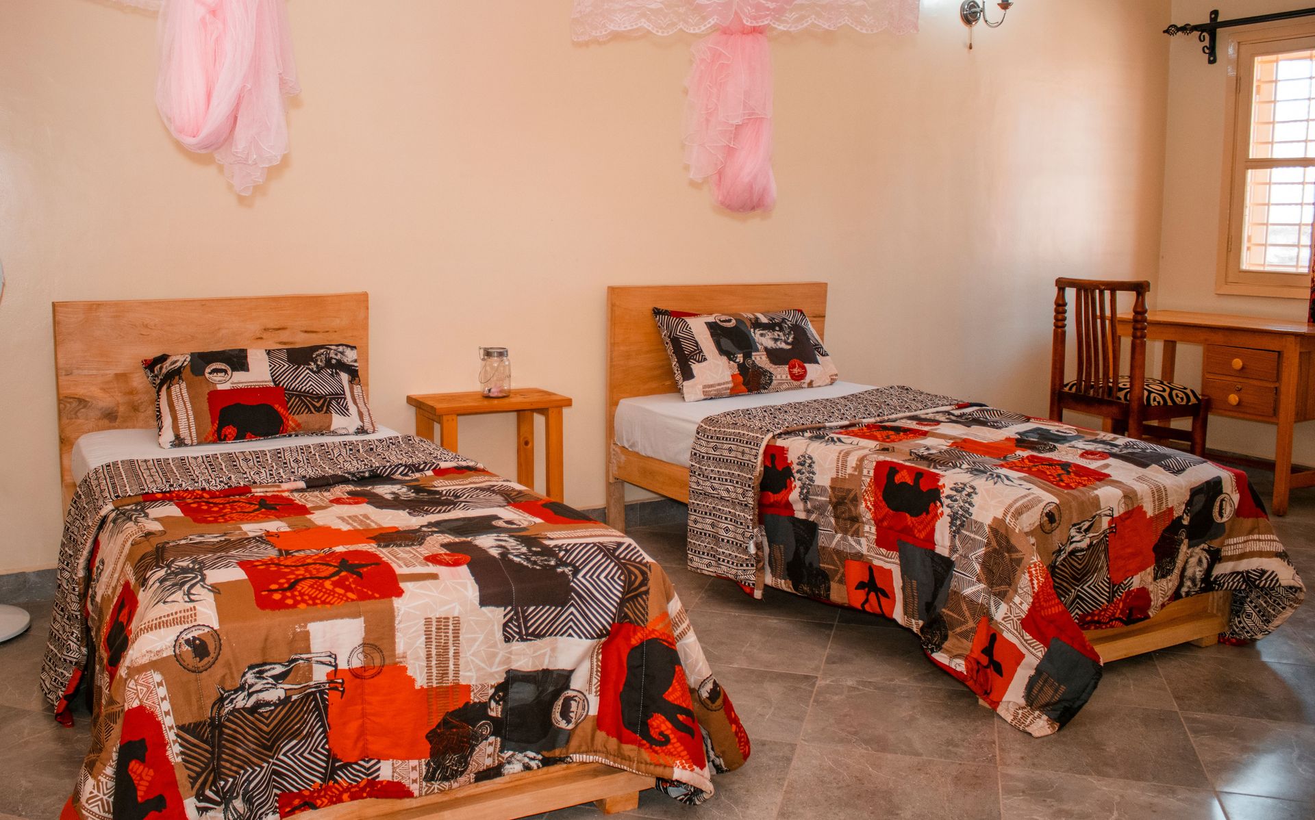Warm, inviting twin bedroom in Kampala with African print quilts and wooden furniture.