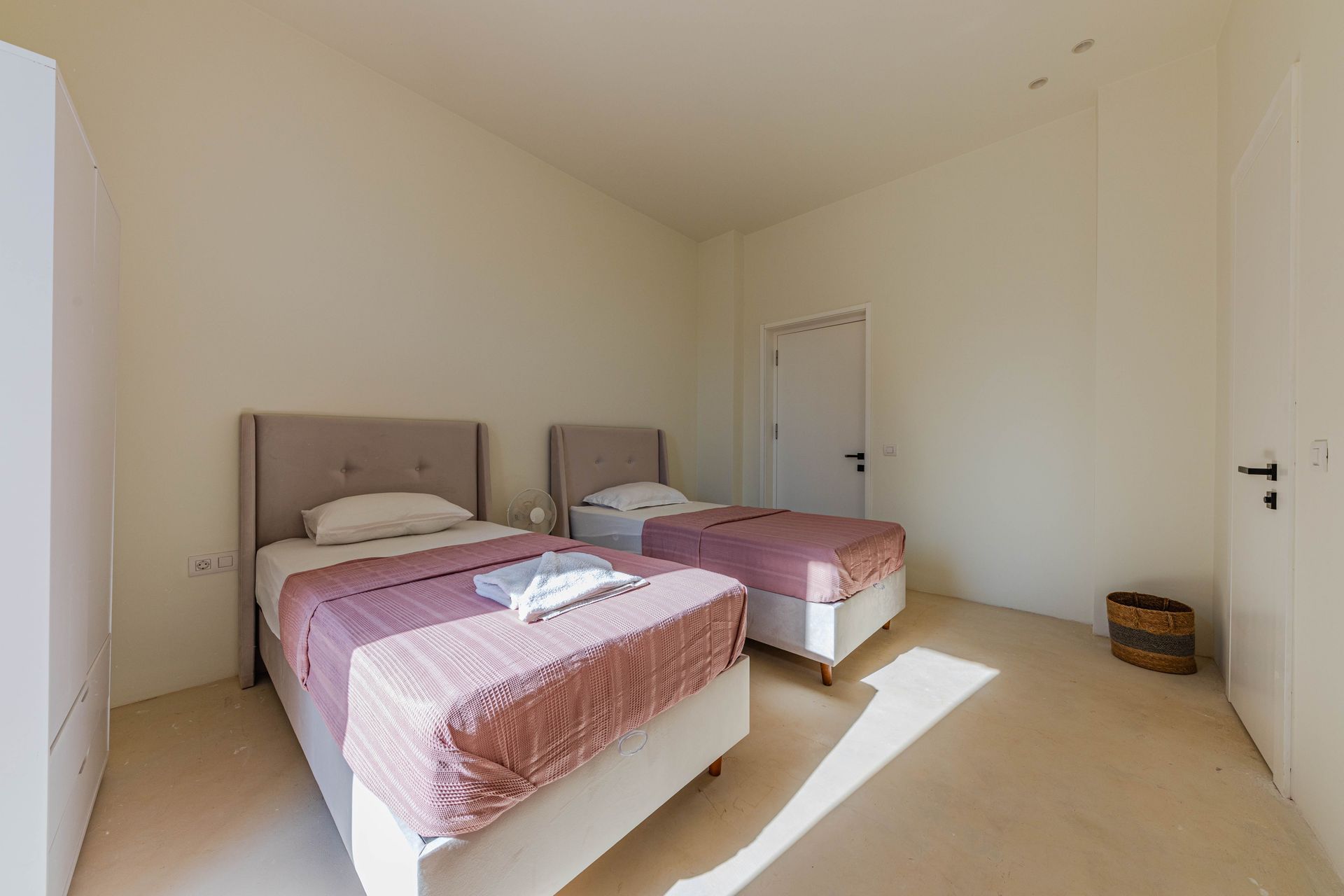 A sunlit minimalist bedroom featuring two twin beds and simple decor.
