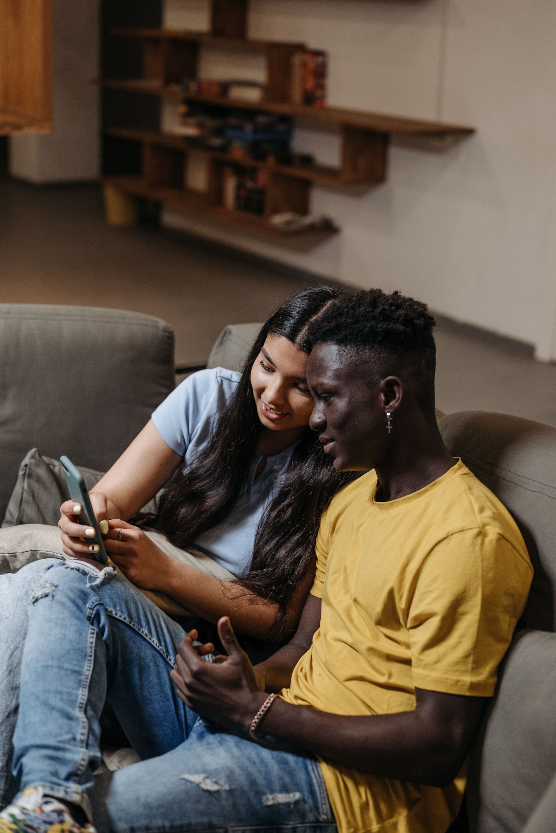 Young couple sitting together on a couch, sharing a moment looking at a smartphone indoors.