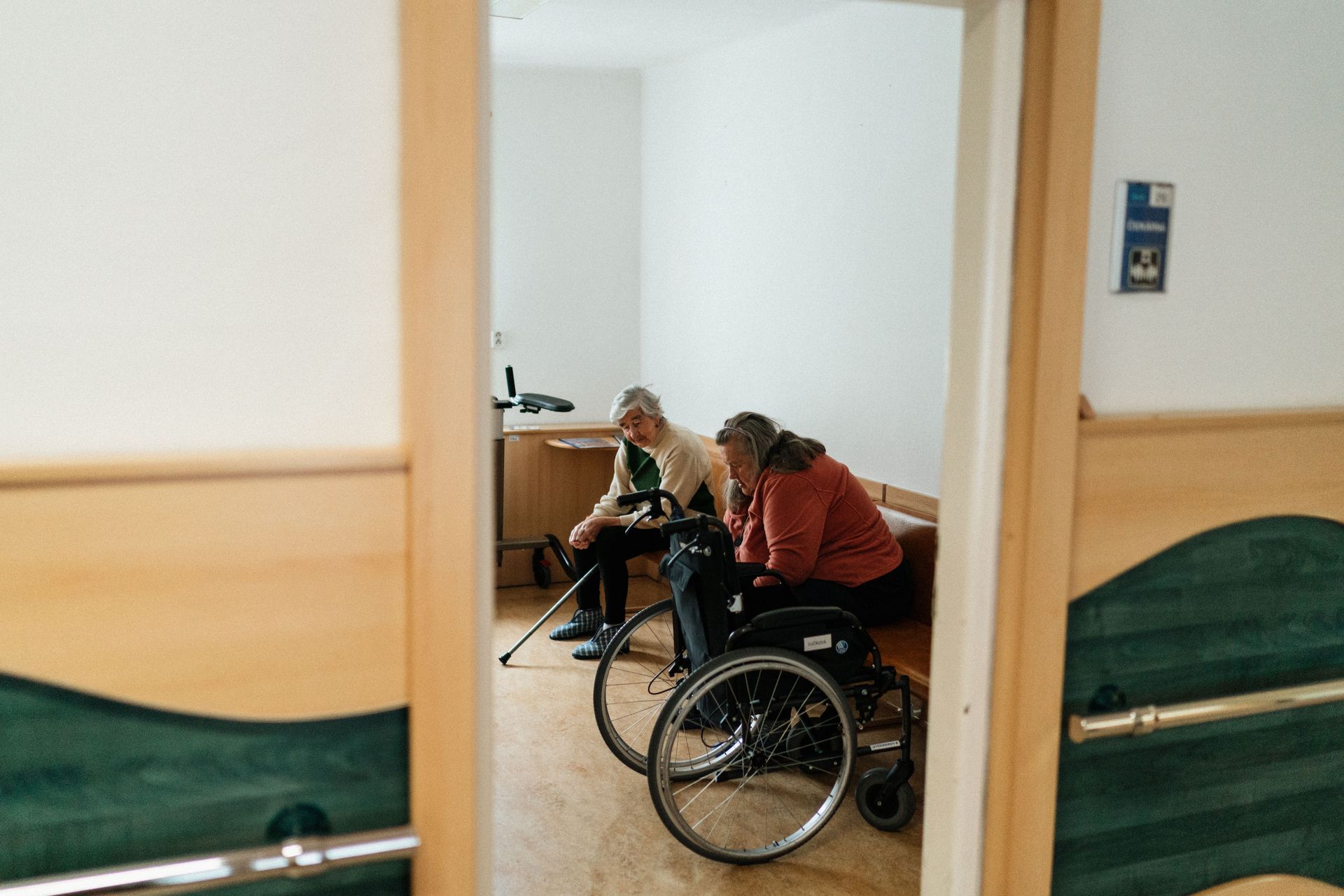 Two senior women conversing indoors, one in a wheelchair, symbolizing companionship in a nursing home setting.